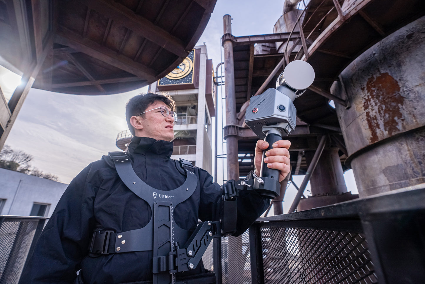 Surveyor using the FJ Dynamics Trion P2/S2 Stabilizing Vest with the Trion S2 to scan outdoor area of industrial factory.