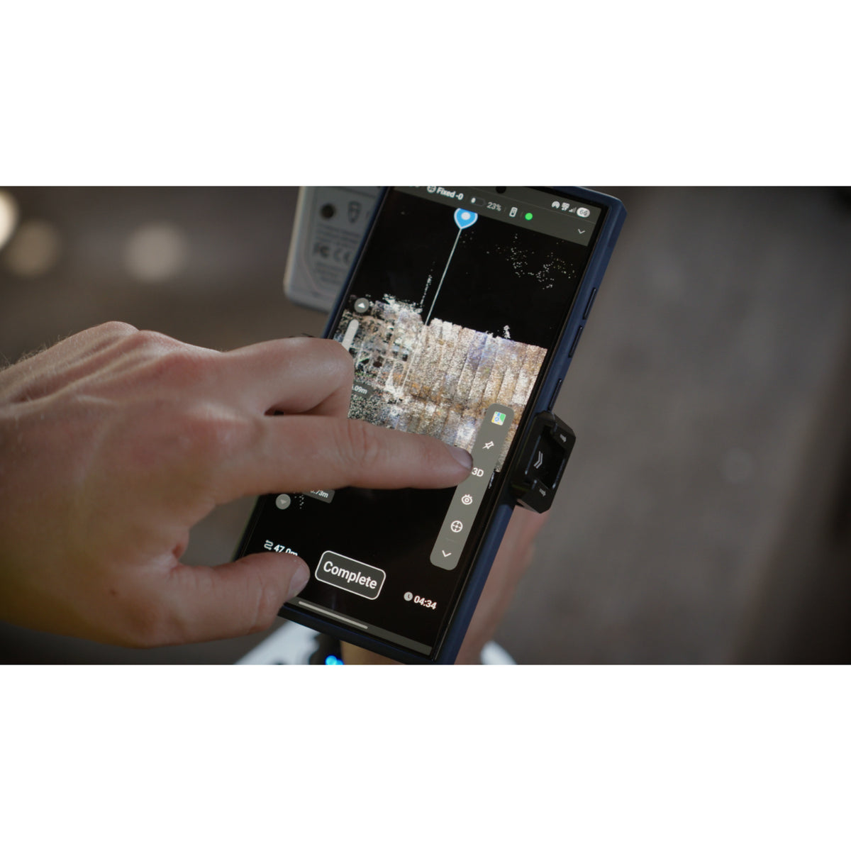 Output from the FJD Trion T1 , A close-up of a hand holding a smartphone in a black protective case, pointing at the screen which displays a detailed inspection or analysis image.