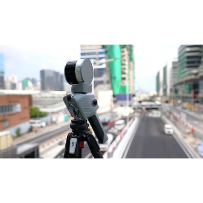 FJD Trion T1 mounted on a tripod for terrestrial laser scanning, surveying. Photographed outdoors with a blurred city street and construction site in the background.