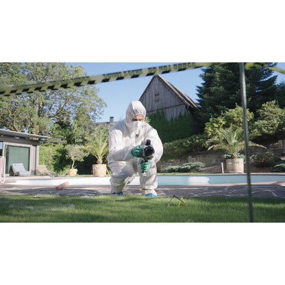 A Forensic Specialist in a white protective hazmat suit and green gloves kneels outdoors near a swimming pool, holding a FJD Trion X1 while capturing the surroundings. The scene includes a house, trees, lawn, and yellow-black caution tape in the foreground.